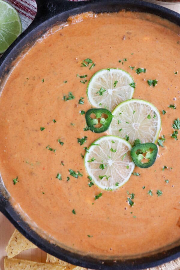 Cheesy dip in a cast iron skillet with three slices of lime, two round slices of jalepeno and fresh parsley for garnish in the center.