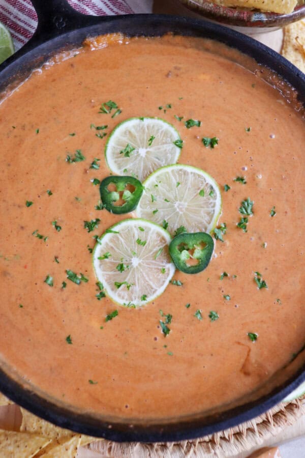 Cheesy dip in a cast iron skillet with three slices of lime, two round slices of jalepeno and fresh parsley for garnish in the center.
