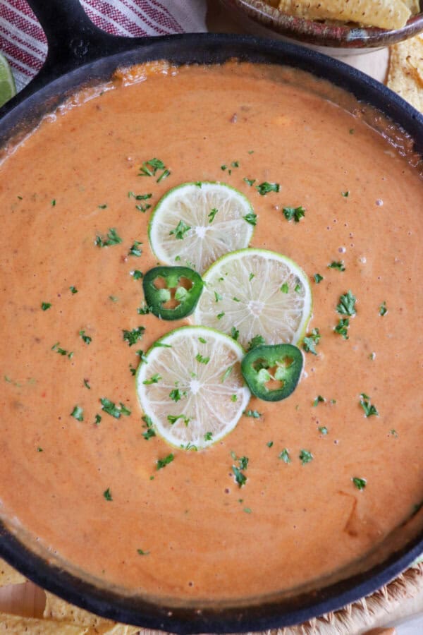 Cheesy dip in a cast iron skillet with three slices of lime, two round slices of jalepeno and fresh parsley for garnish in the center.