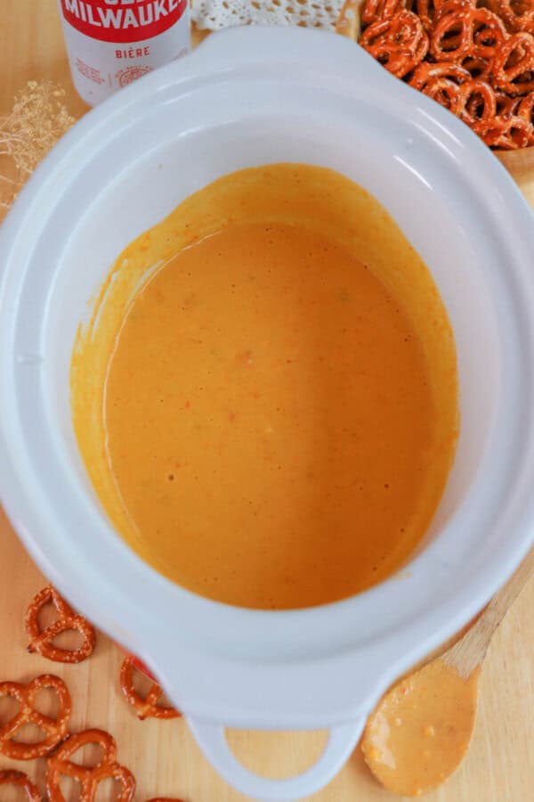 Cheese dip in a small white crockpot surrounded by pretzels.
