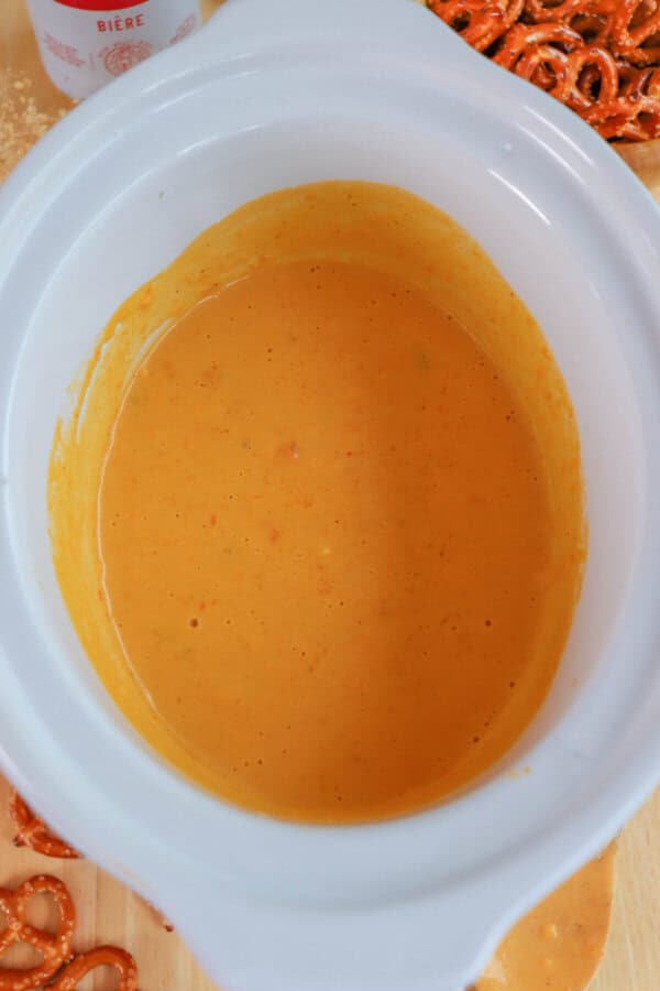 Cheese dip in a small white crockpot surrounded by pretzels.