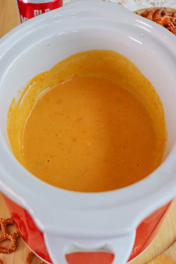 Cheese dip in a small white crockpot surrounded by pretzels.