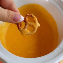 A pretzel being dipped in cheese sauce.