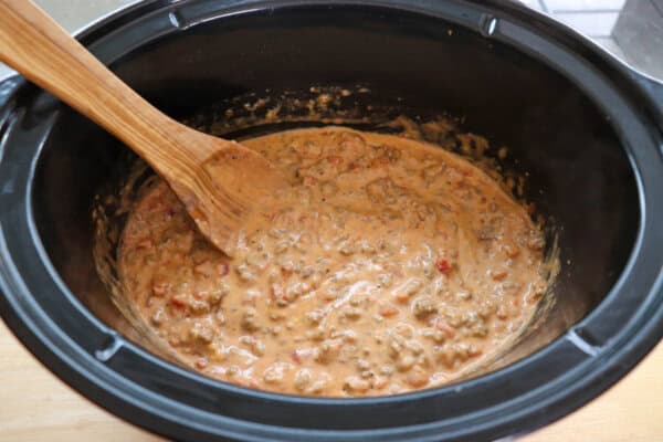 Creamy cheese dip with diced tomatoes and ground beef in a black crockpot.