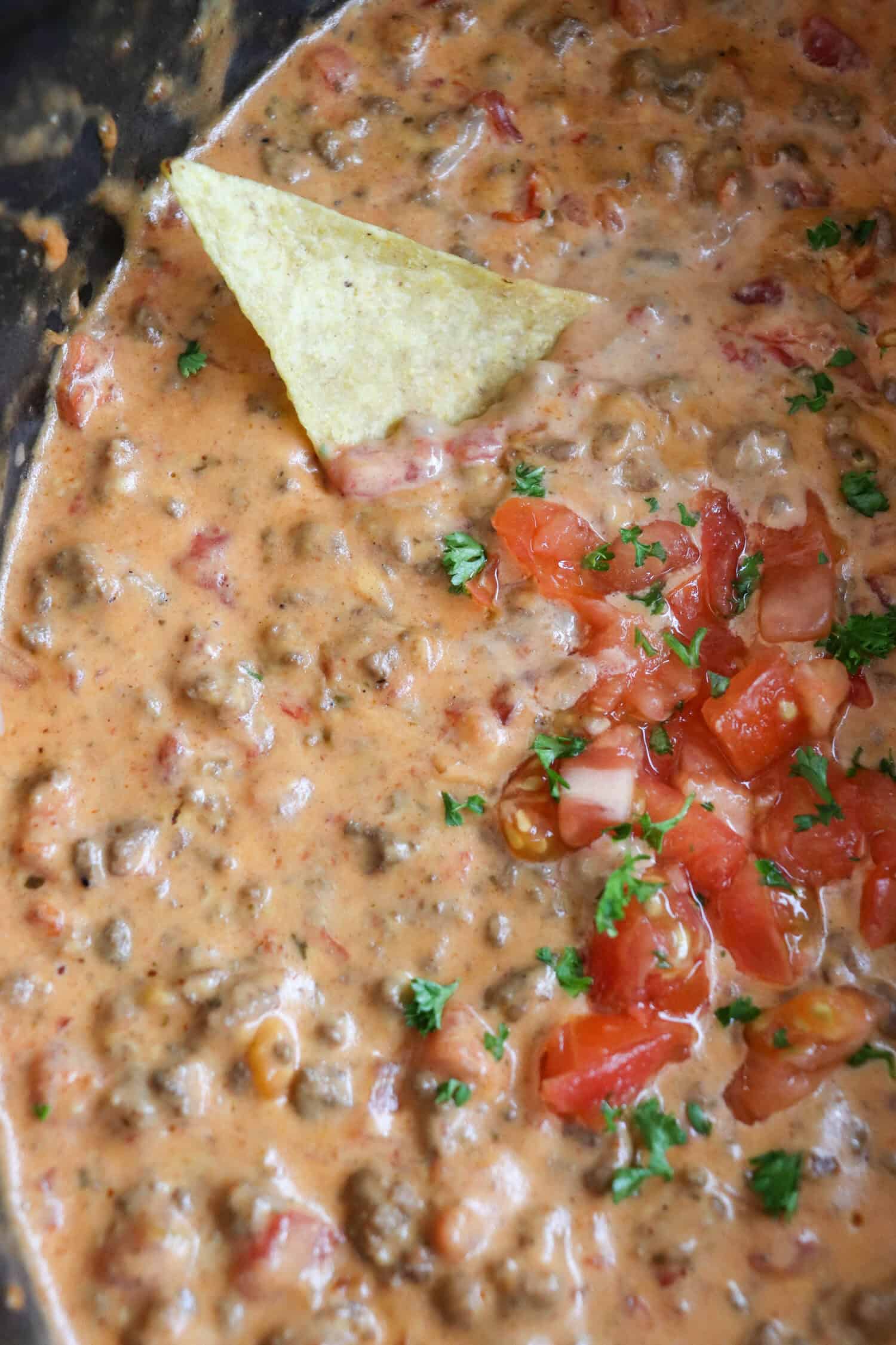 Cheesy rotel dip with diced tomatoes and ground beef in a black crockpot with a tortilla dip resting inside.