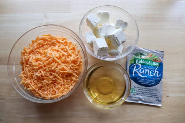 Ingredients for beer ranch cheese dip in clear bowls on a wooden table.