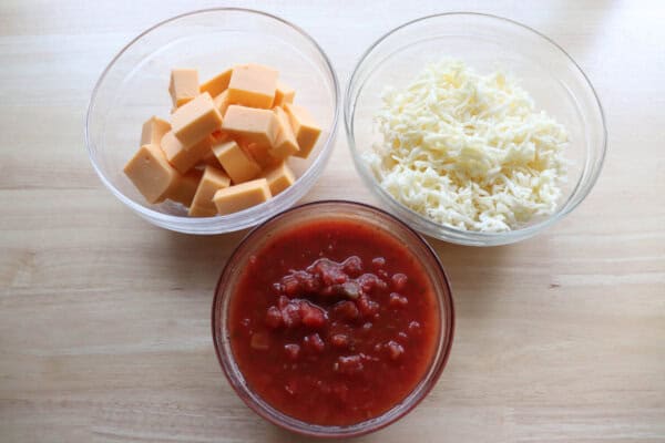 Ingredients for meatless Rotel dip in clear glass bowls on a wooden table.