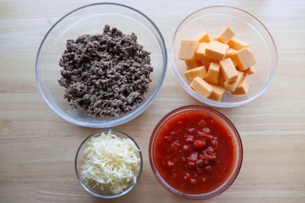Cheesy rotel dip ingredients in clear bowls on a wooden table.