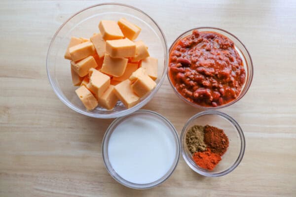 Skillet queso dip ingredients in clear glass bowls on a wooden table.