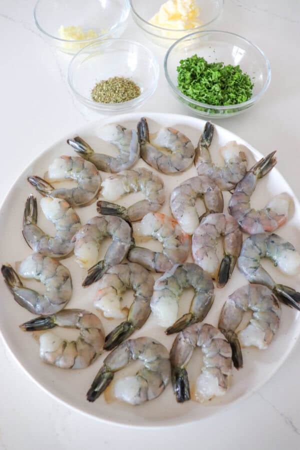 Ingredients for garlic butter shrimp in clear glass bowls with prepared raw shrimp on a white plate.