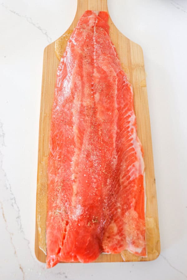 Large salmon fillet on a cutting boards with melted butter coating the top.