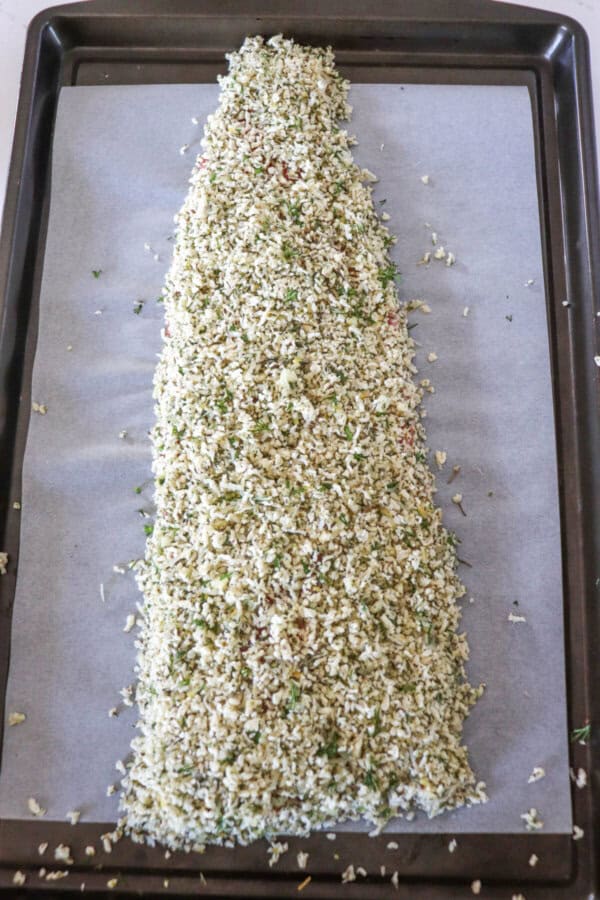 Large salmon on a baking sheet with a breadcrumb mixture coating the top.