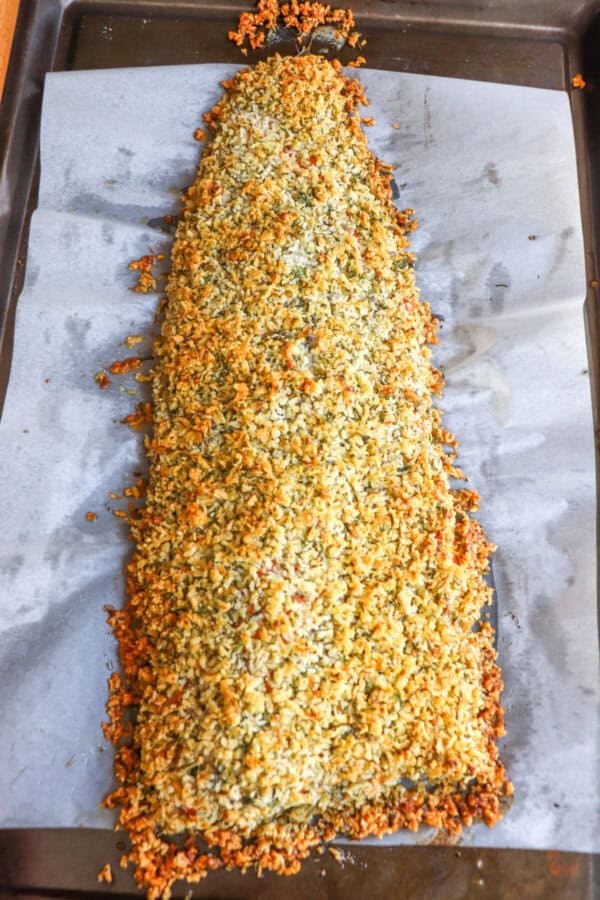 Large salmon on a baking sheet with a breadcrumb mixture coating the top.