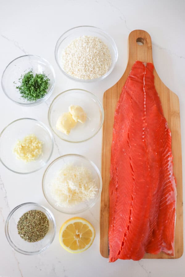 Ingredients for herb crusted salmon in clear glass bowls on a white counter.