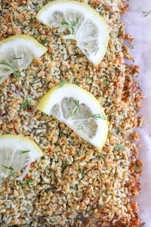 Salmon fillet covered in a crust of panko and herbs on a sheet of parchment paper topped with lemon slices for garnish.