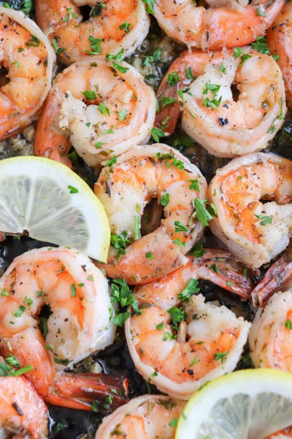 Cooked shrimp in garlic and butter on a cast iron skillet with fresh parsley and lemon slices for garnish.