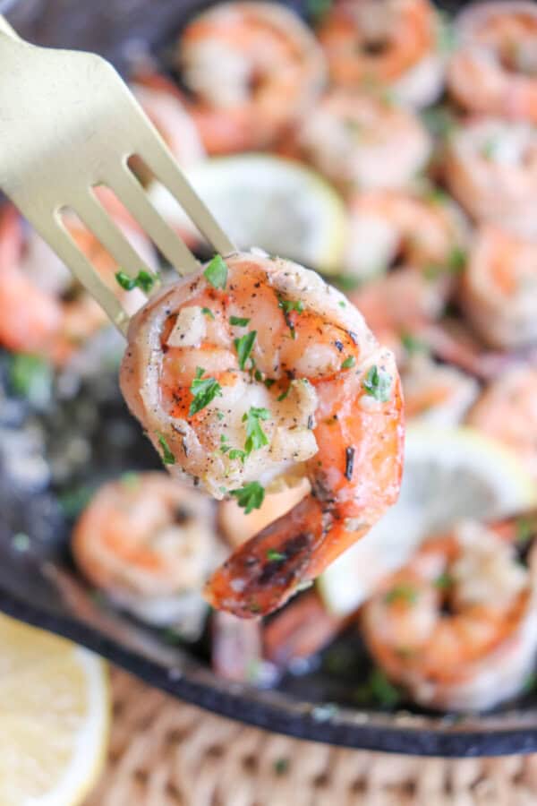 Cooked shrimp on a fork with fresh parsley and garlic.