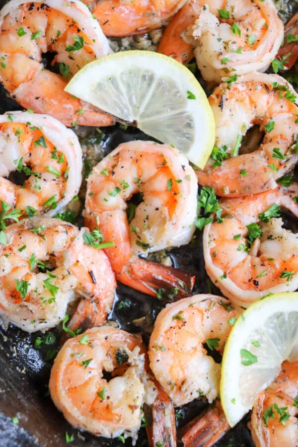 Cooked shrimp in garlic and butter on a cast iron skillet with fresh parsley and lemon slices for garnish.