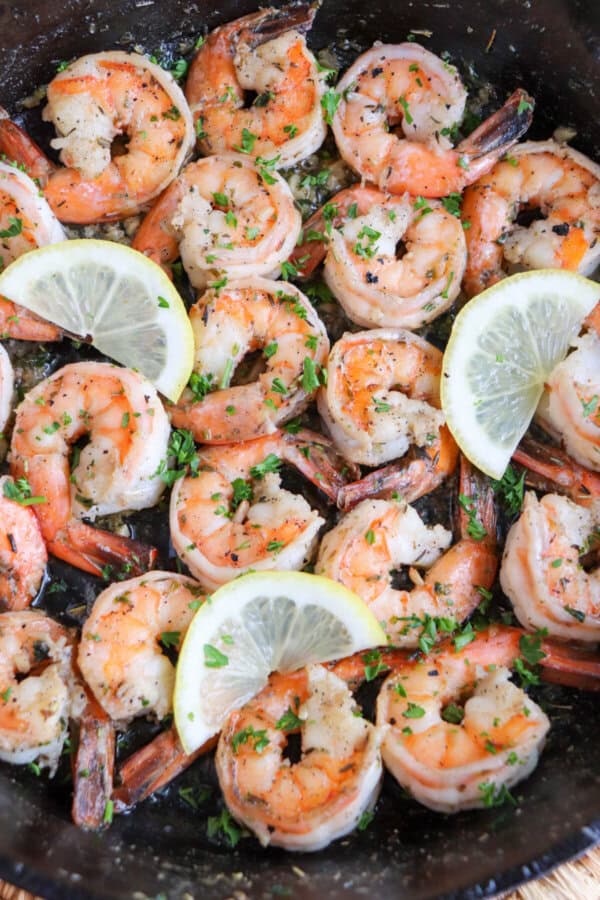 Cooked shrimp in garlic and butter on a cast iron skillet with fresh parsley and lemon slices for garnish.