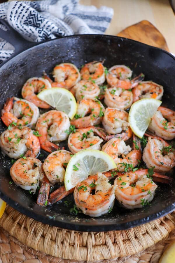 Cooked shrimp in garlic and butter on a cast iron skillet with fresh parsley and lemon slices for garnish.