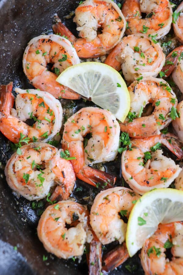 Cooked shrimp in garlic and butter on a cast iron skillet with fresh parsley and lemon slices for garnish.