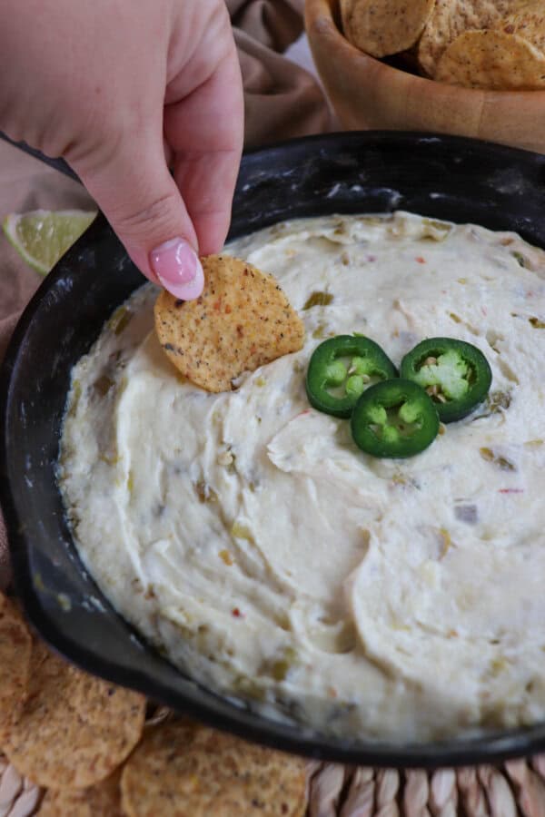 White pepper jack cheese dip in a cast iron skillet topped with three slices of jalapeno pepper with a tortilla being dipped into the cheese.