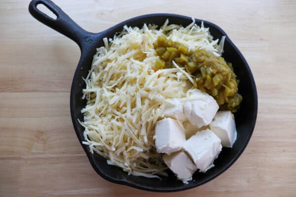 Cubed cream cheese, shredded pepper jack cheese and diced chilis in a cast iron skillet.