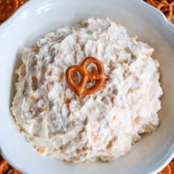 Creamy ranch beer cheese dip in a white bowl, surrounded by pretzels and crackers with a pretzel on top.