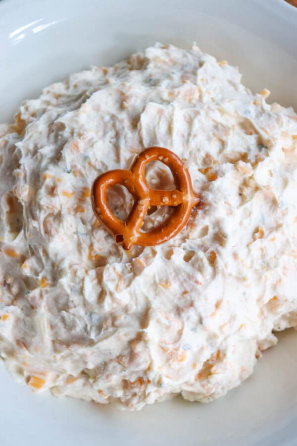 Creamy ranch beer cheese dip in a white bowl, surrounded by pretzels and crackers with a pretzel on top.