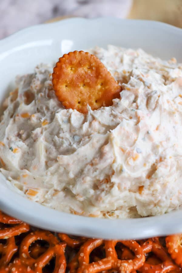 Close up of creamy ranch beer cheese dip in a white bowl, surrounded by pretzels and crackers with a pretzel cracker on top.