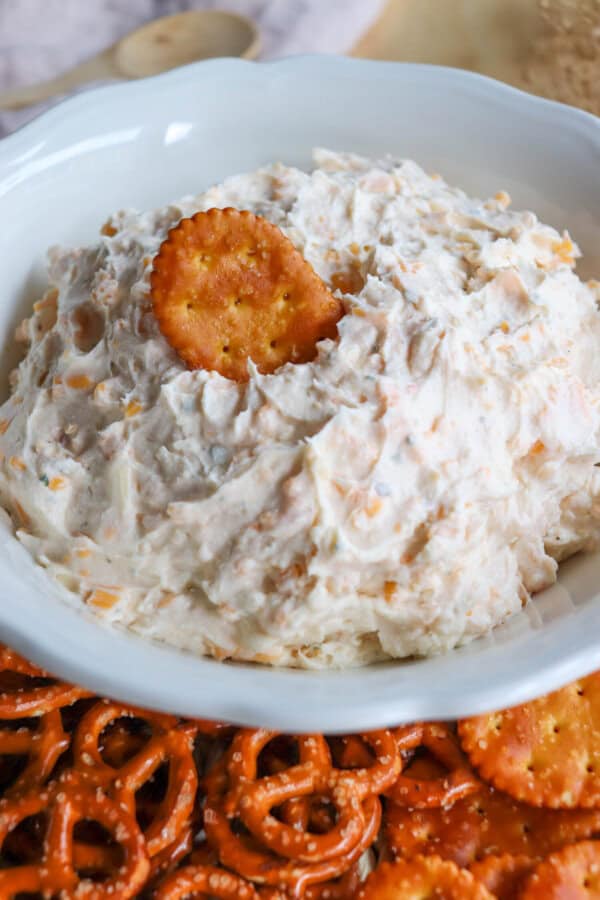 Close up of creamy ranch beer cheese dip in a white bowl, surrounded by pretzels and crackers with a pretzel cracker on top.