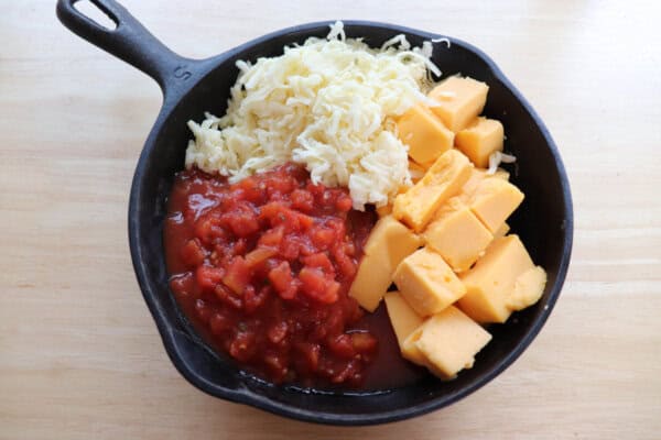 Ingredients for meatless Rotel dip in a cast iron skillet on a wooden table.
