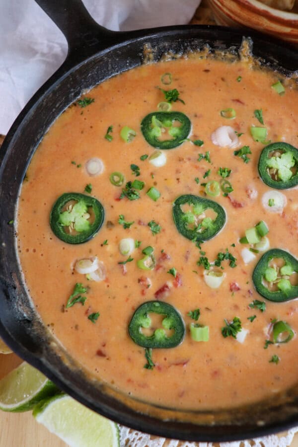 Cheesy rotel dip with no meat in a cast iron skillet topped with sliced jalapenos and diced green onions.