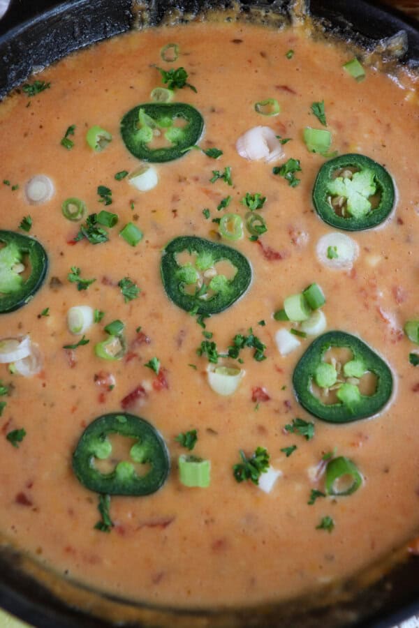 Close up of cheesy rotel dip with no meat in a cast iron skillet topped with sliced jalapenos and diced green onions.