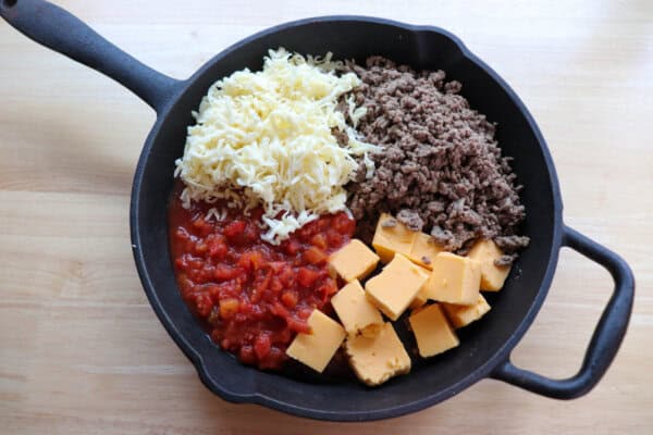 Rotel dip ingredients in a large cast iron skillet on a wood table.