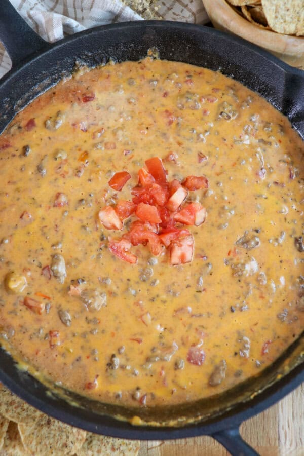 Creamy cheese dip with ground beef and tomatoes in a cast iron skillet topped with fresh diced tomatoes in the center.