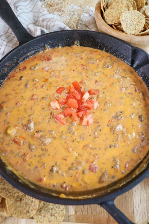 Creamy cheese dip with ground beef and tomatoes in a cast iron skillet topped with fresh diced tomatoes in the center.