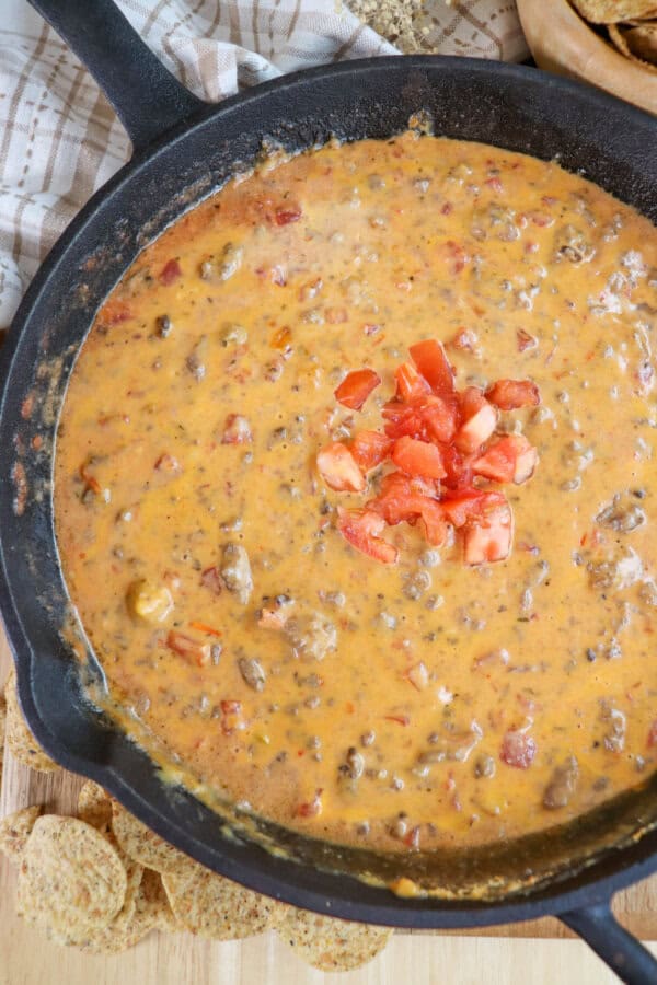 Creamy cheese dip with ground beef and tomatoes in a cast iron skillet topped with fresh diced tomatoes in the center.