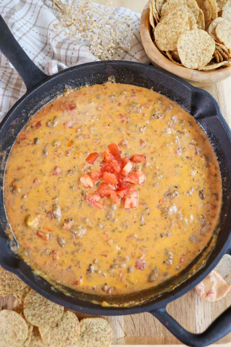 Creamy cheese dip with ground beef mixed and melted in a skillet topped with diced tomatoes and surrounded by round tortilla chips.