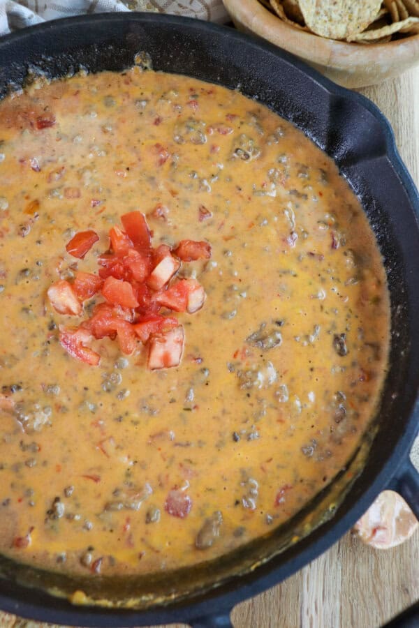 Creamy cheese dip with ground beef and tomatoes in a cast iron skillet topped with fresh diced tomatoes in the center.