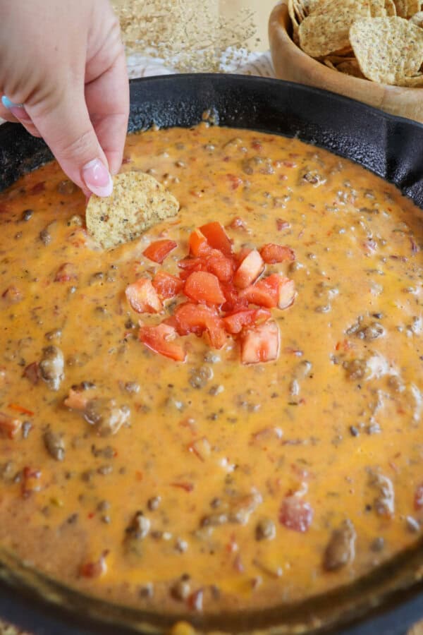 Creamy cheese dip with ground beef and tomatoes in a cast iron skillet topped with fresh diced tomatoes in the center with a round tortilla being dipped.
