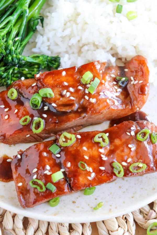 Salmon fillets covered in a brown sugar & bourbon glaze on a white plate with green onion and sesame seeds garnishing the fish.