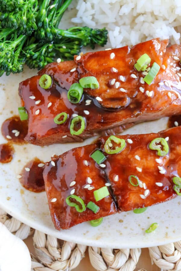 Salmon fillets covered in a brown sugar & bourbon glaze on a white plate with green onion and sesame seeds garnishing the fish.