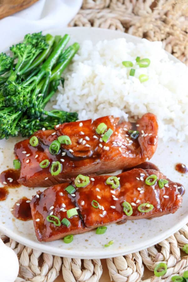 Salmon fillets covered in a brown sugar & bourbon glaze on a white plate with green onion and sesame seeds garnishing the fish.