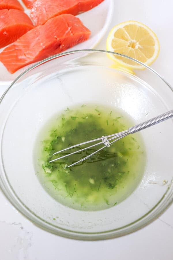 Salmon lemon marinade ingredients mixed in a clear glass bowl with a small whisk.