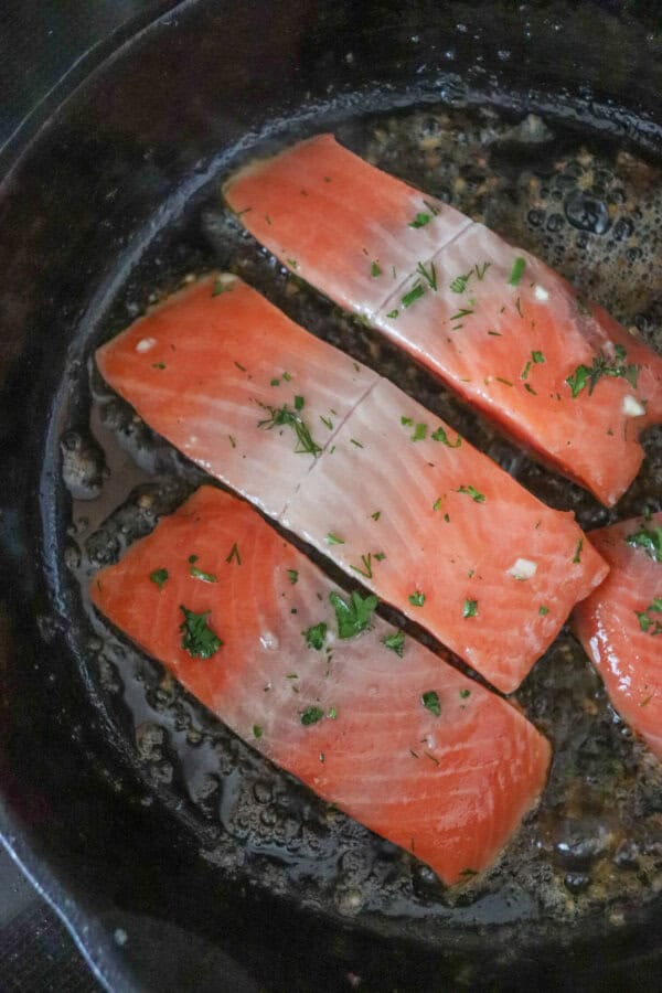 Three raw salmon filets in a cast iron skillet.