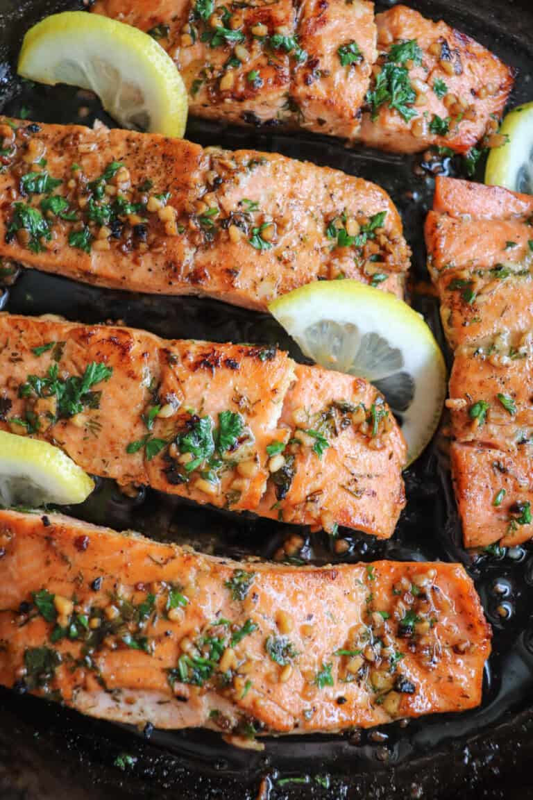 Salmon fillets in a cast iron skillet topped with fresh parsley and lemon slices.