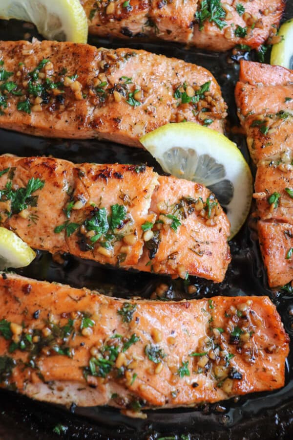 Salmon fillets in a cast iron skillet topped with fresh parsley and lemon slices.
