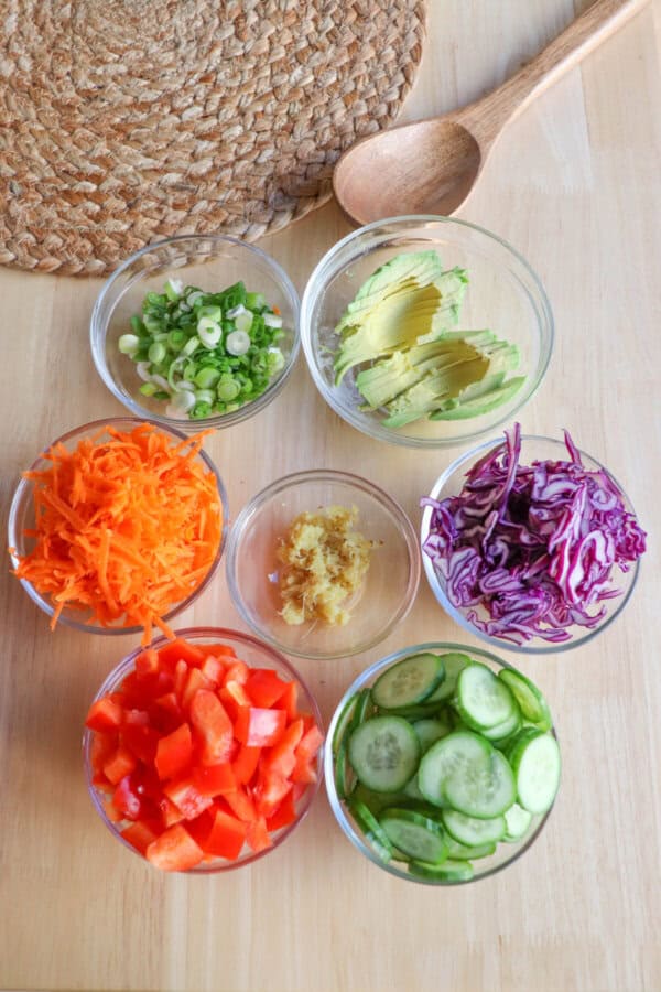 Ingredients for salmon poke bowl in clear glass bowls on a wooden table.