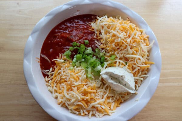 Salsa, shredded cheese, cream cheese and diced green onion in a large white circular baking dish.